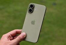 iPhone 17 màu xanh được cầm trên tay ngoài trời, thấy rõ cụm camera kép ở mặt lưng.