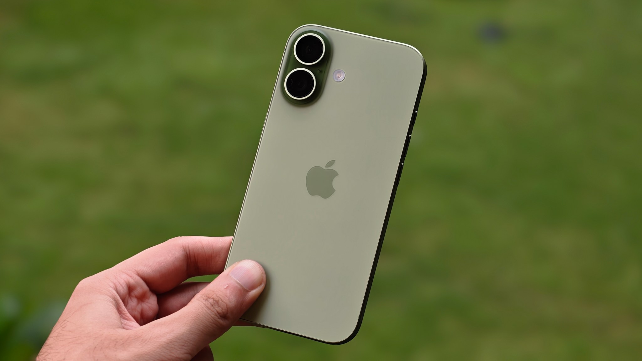 iPhone 17 màu xanh được cầm trên tay ngoài trời, thấy rõ cụm camera kép ở mặt lưng.