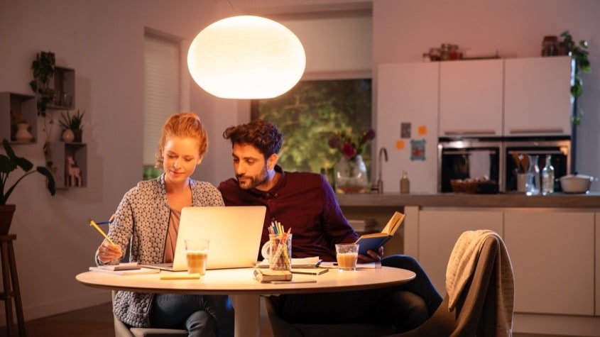 Hai người làm việc với laptop dưới nguồn sáng trong không gian gia đình; hướng và độ mềm của ánh sáng ảnh hưởng khung hình webcam. Ảnh: Philips Hue.