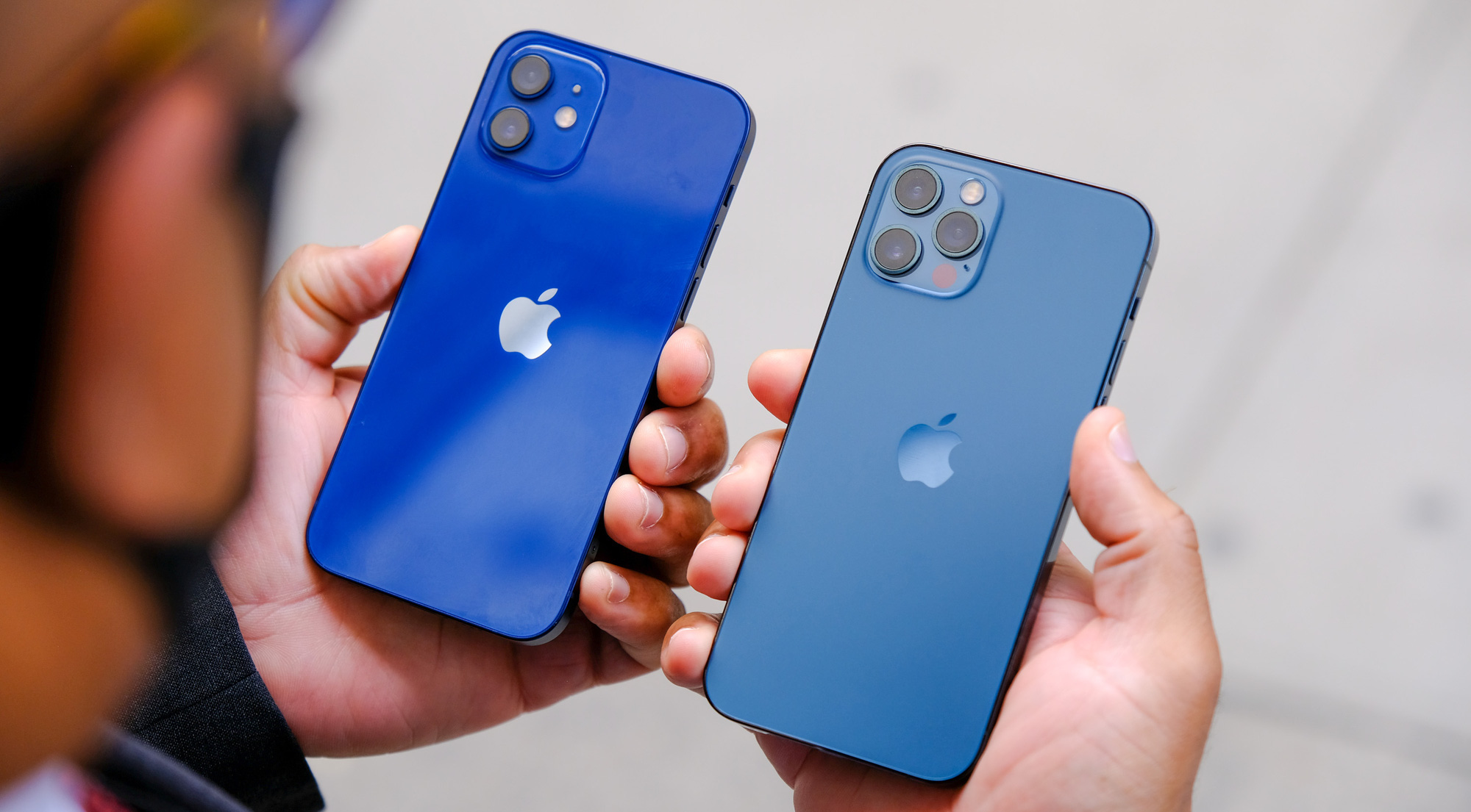 Hai iPhone màu xanh được cầm trên tay, một máy có cụm ba camera