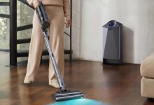 Người dùng đang điều khiển máy hút bụi Narwal V50 Cube với đèn soi bụi trên sàn gỗ cạnh trạm sạc