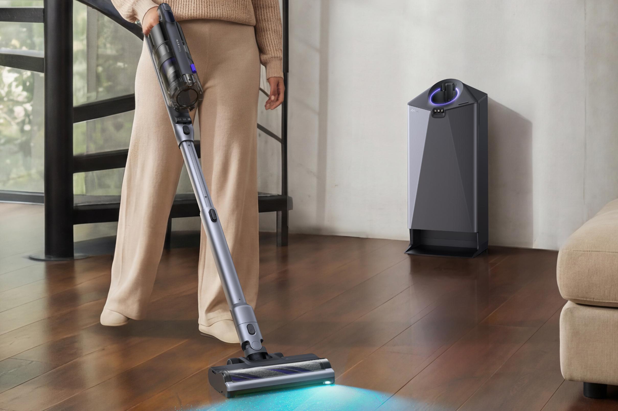 Người dùng đang điều khiển máy hút bụi Narwal V50 Cube với đèn soi bụi trên sàn gỗ cạnh trạm sạc