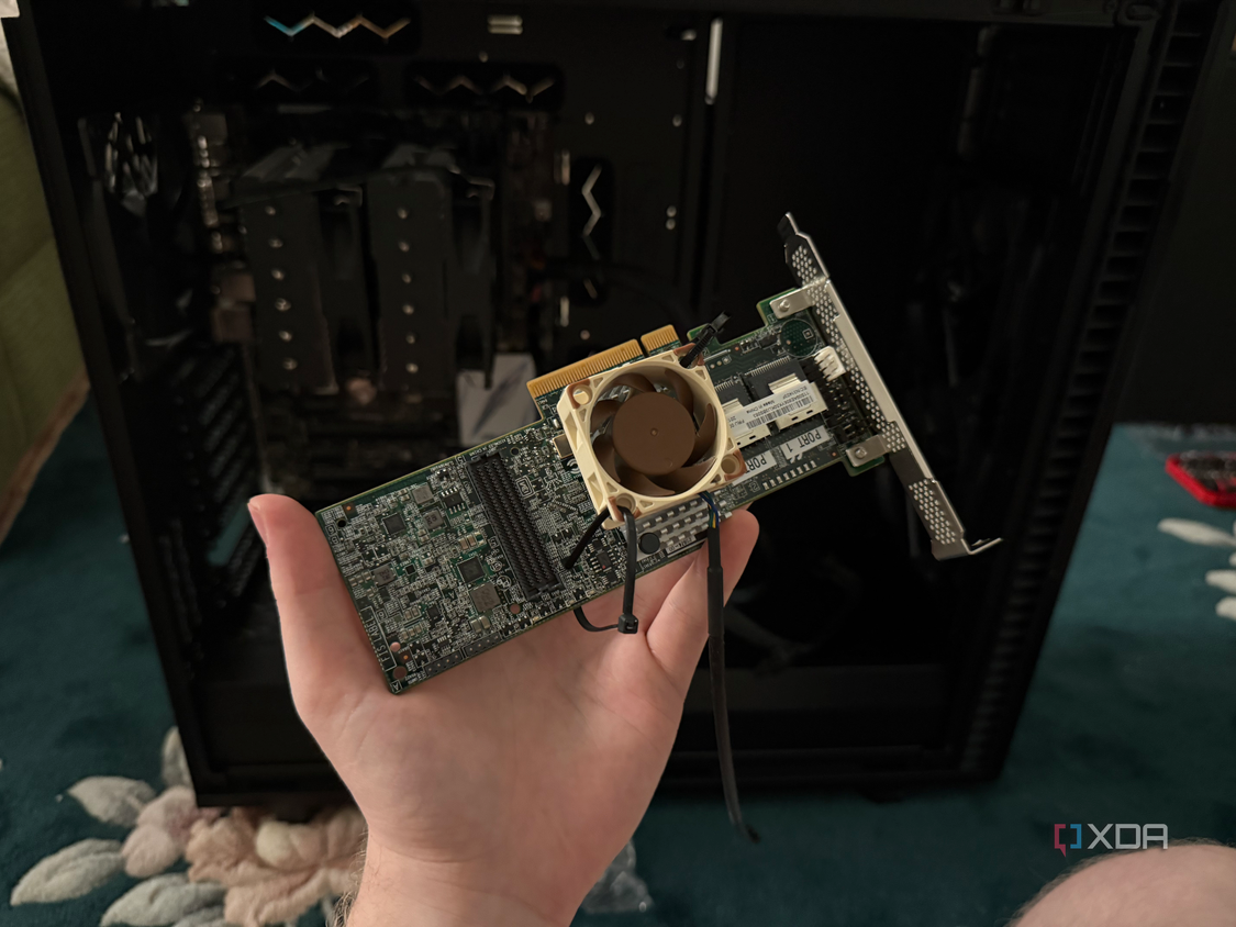 A photo of someone holding a SAS PCIe card with a Noctua fan ziptied to it