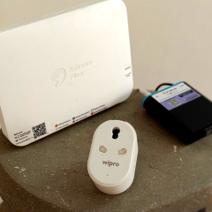 A white Wi-Fi router on a grey surface next to a smart plug and a mini UPS