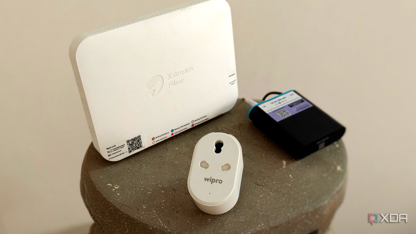 A white Wi-Fi router on a grey surface next to a smart plug and a mini UPS