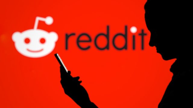 Bóng người dùng smartphone trước logo Reddit màu đỏ
