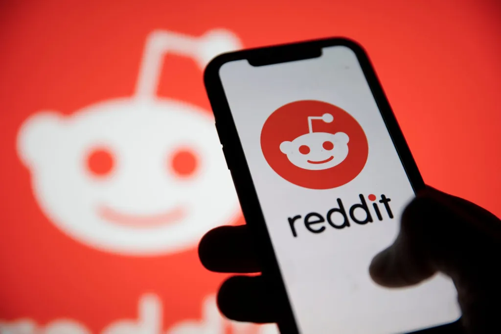 Điện thoại hiển thị biểu tượng Reddit trước nền logo cùng dịch vụ.
