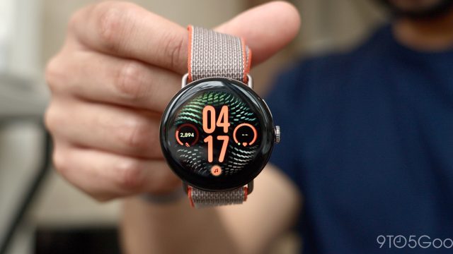 Đồng hồ Pixel Watch mặt tròn, dây vải được cầm trước máy ảnh