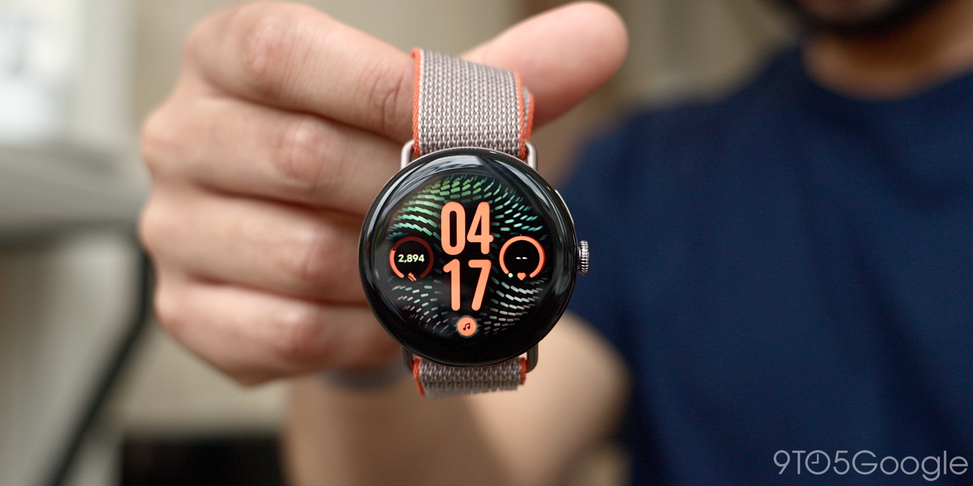Đồng hồ Pixel Watch mặt tròn, dây vải được cầm trước máy ảnh