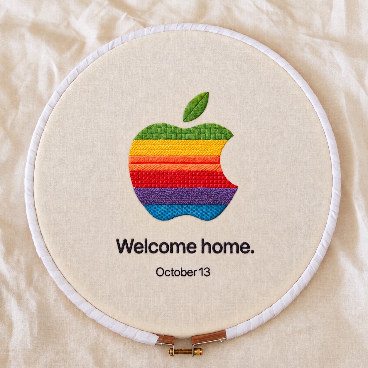 Logo Apple nhiều màu được khâu trên nền vải cùng dòng chữ Welcome home và October 13