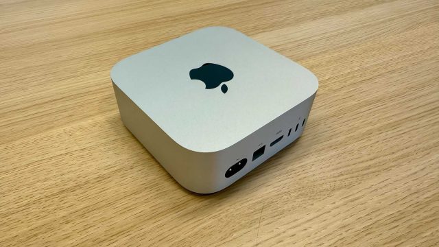 Mac mini màu bạc đặt trên bàn gỗ, thấy mặt sau có cổng HDMI và Thunderbolt