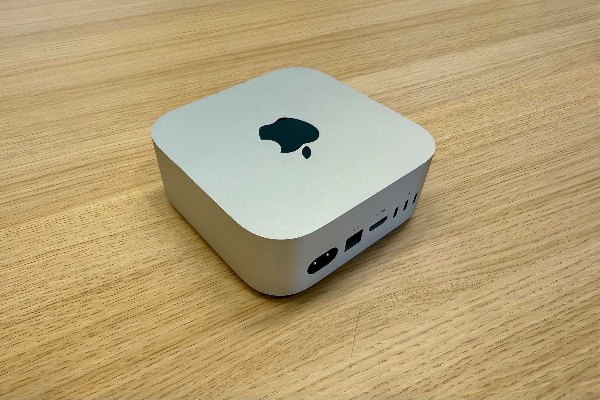 Mac mini màu bạc đặt trên bàn gỗ, thấy mặt sau có cổng HDMI và Thunderbolt