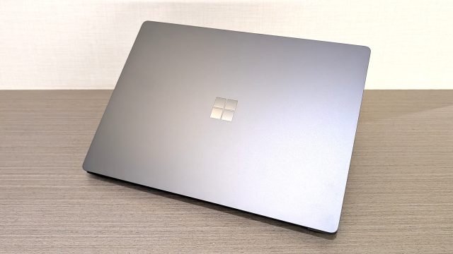 Mặt trên màu Platinum của laptop Surface khép kín, đặt trên bàn gỗ.