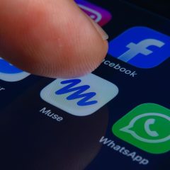 Ngón tay chọn biểu tượng Muse trên điện thoại, cạnh biểu tượng Facebook và WhatsApp.