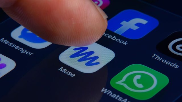 Ngón tay chọn biểu tượng Muse trên điện thoại, cạnh biểu tượng Facebook và WhatsApp.