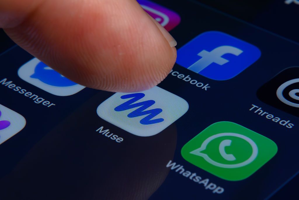 Ngón tay chọn biểu tượng Muse trên điện thoại, cạnh biểu tượng Facebook và WhatsApp.