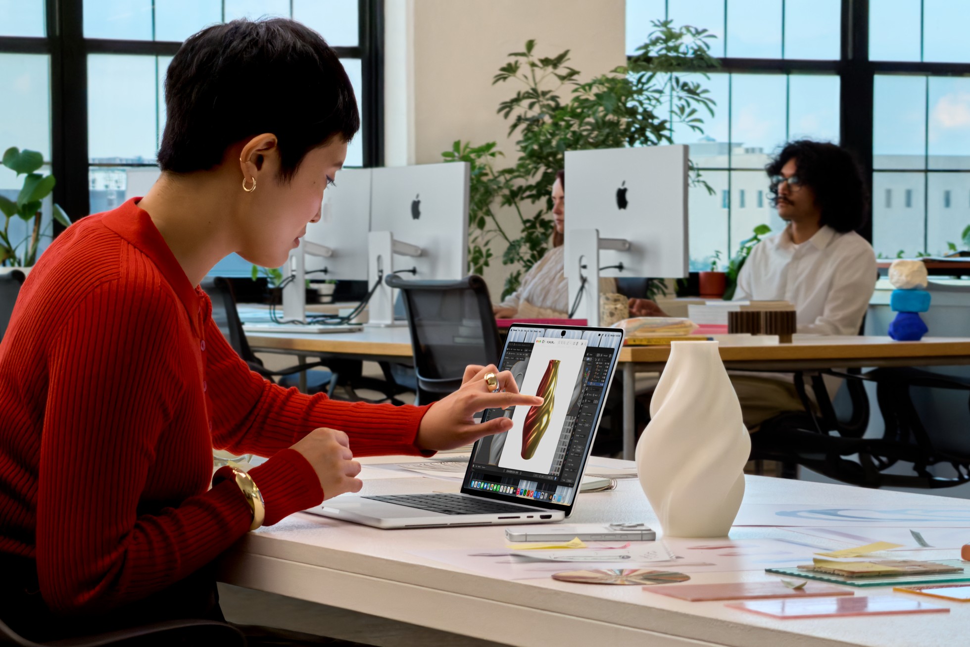 Người dùng chạm mô hình thiết kế trên MacBook Pro tại bàn làm việc.