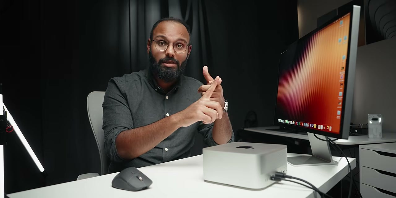 Người dẫn chương trình ngồi cạnh Mac Studio trên bàn làm việc.