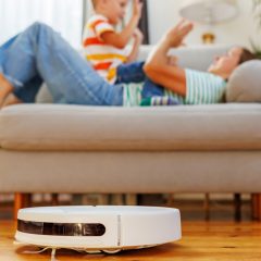 Robot hút bụi chạy trong phòng khách có người lớn và trẻ nhỏ