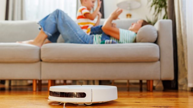 Robot hút bụi chạy trong phòng khách có người lớn và trẻ nhỏ