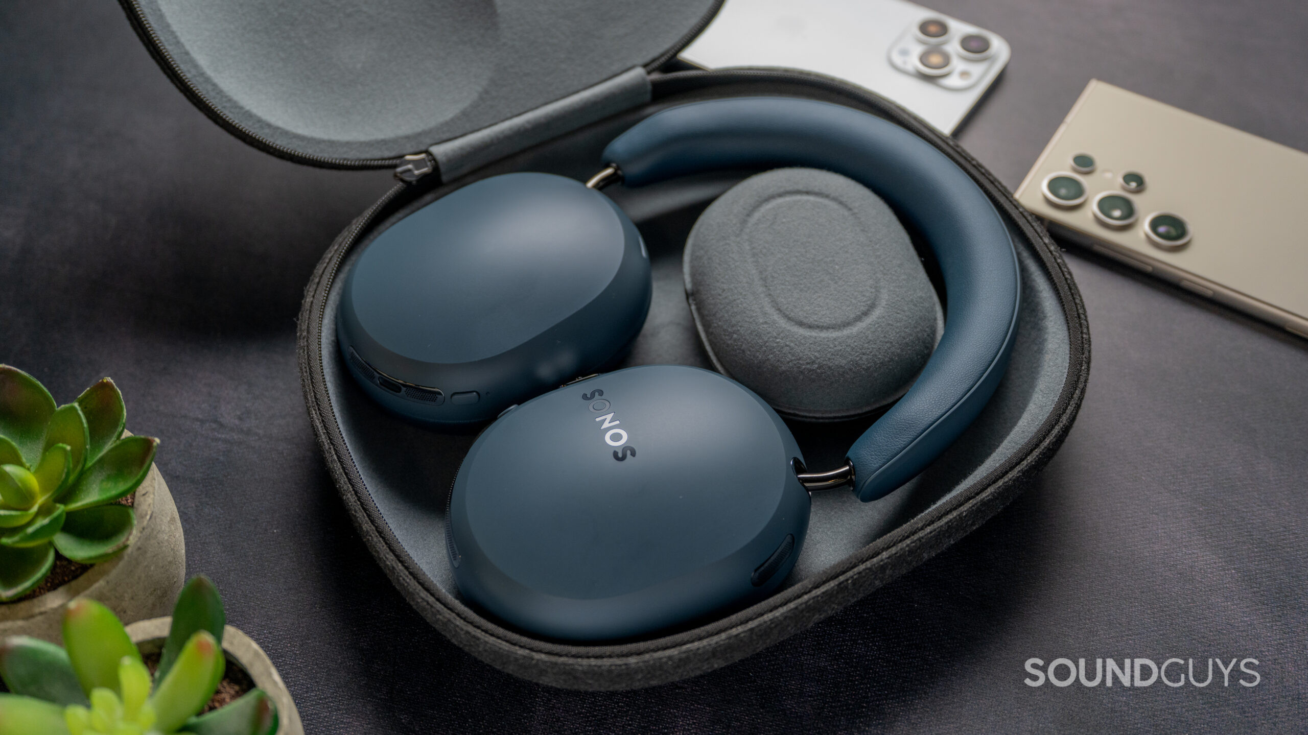 Sonos Ace Ultra inside case with plants and phones next to the headphones.