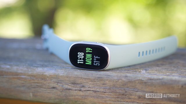 Vòng đeo Fitbit Edge đặt trên mặt bàn gỗ ngoài trời.