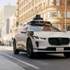 Xe tự hành Waymo màu trắng gắn cảm biến di chuyển trên đường phố
